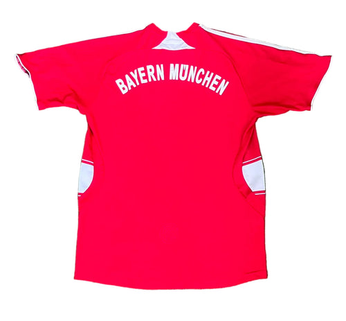 A red short-sleeve Bayern Munich soccer jersey with white trim and 'BAYERN MÜNCHEN' printed in white across the chest