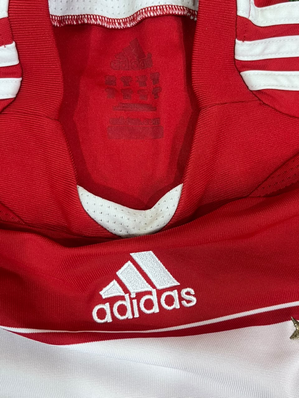 Close-up of a red Adidas sports jersey with white stripes and the white Adidas logo on the chest.