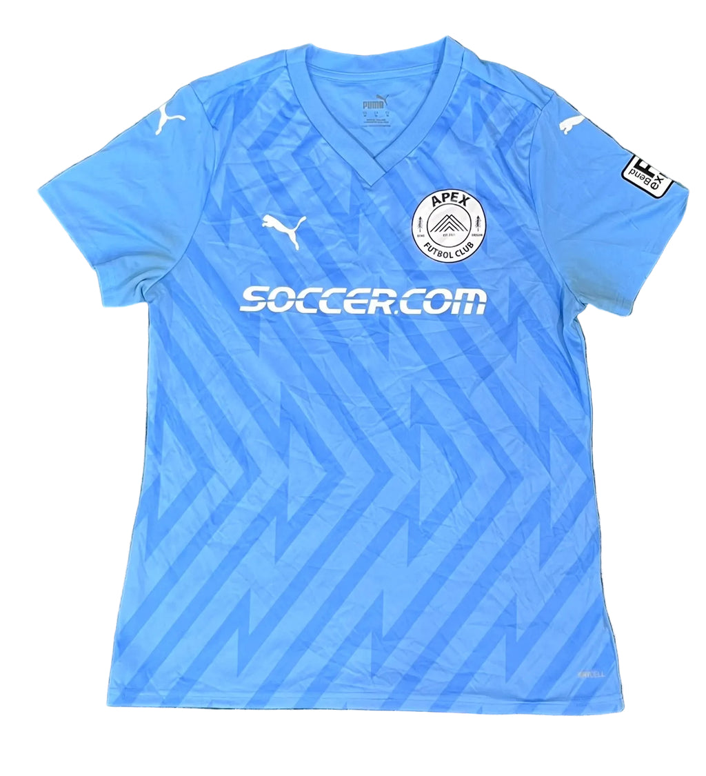 A light blue Puma APEX Football Club soccer jersey The jersey features a V-neck, a subtle geometric pattern, the Puma logo on the chest and shoulders, the APEX Football Club crest, and the 'SOCCER.