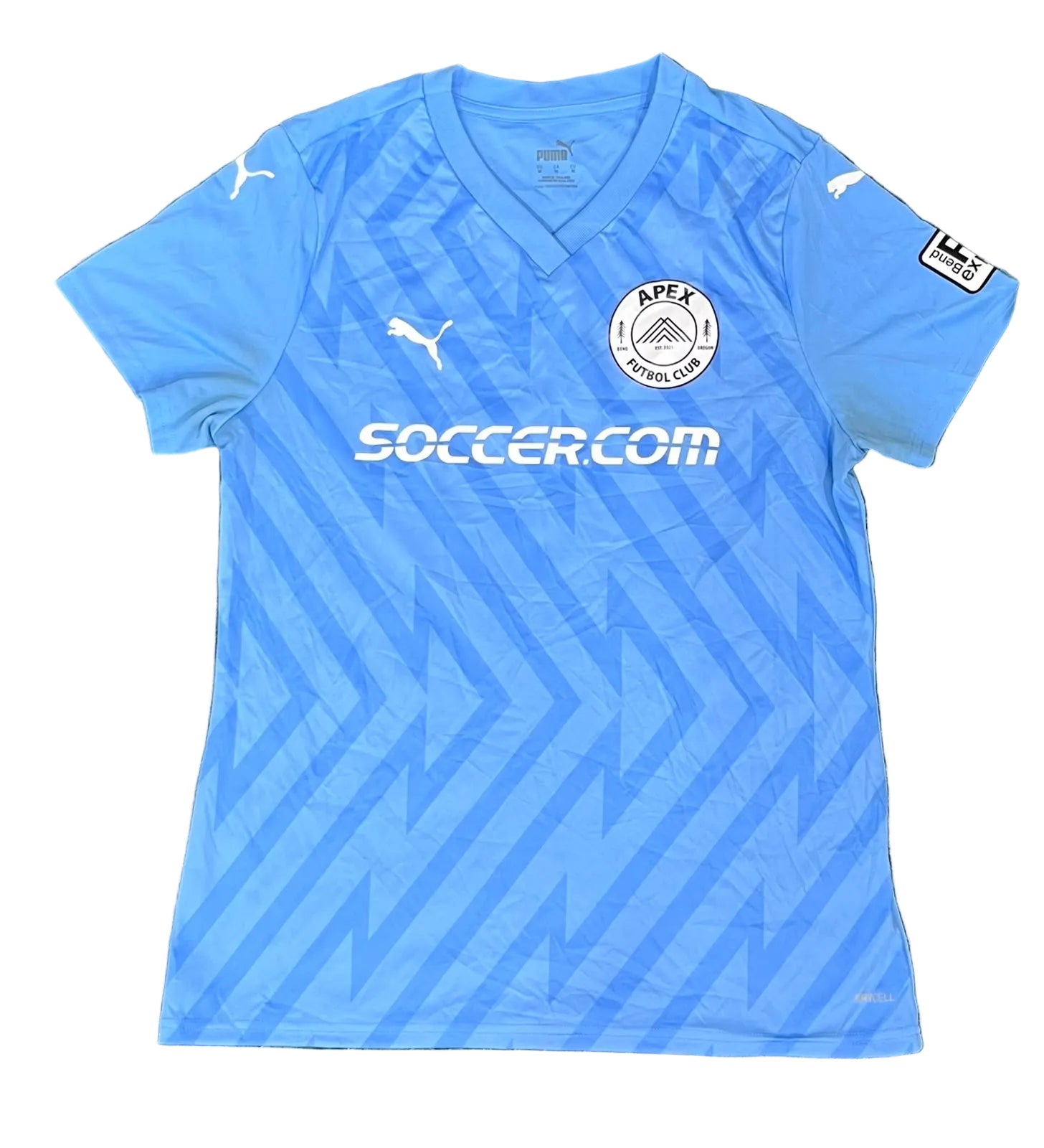 A light blue Puma APEX Football Club soccer jersey The jersey features a V-neck, a subtle geometric pattern, the Puma logo on the chest and shoulders, the APEX Football Club crest, and the 'SOCCER.