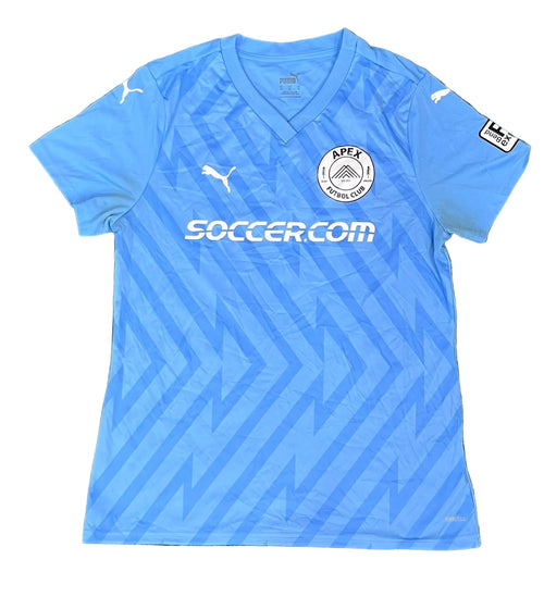 A light blue Puma APEX Football Club soccer jersey The jersey features a V-neck, a subtle geometric pattern, the Puma logo on the chest and shoulders, the APEX Football Club crest, and the 'SOCCER.