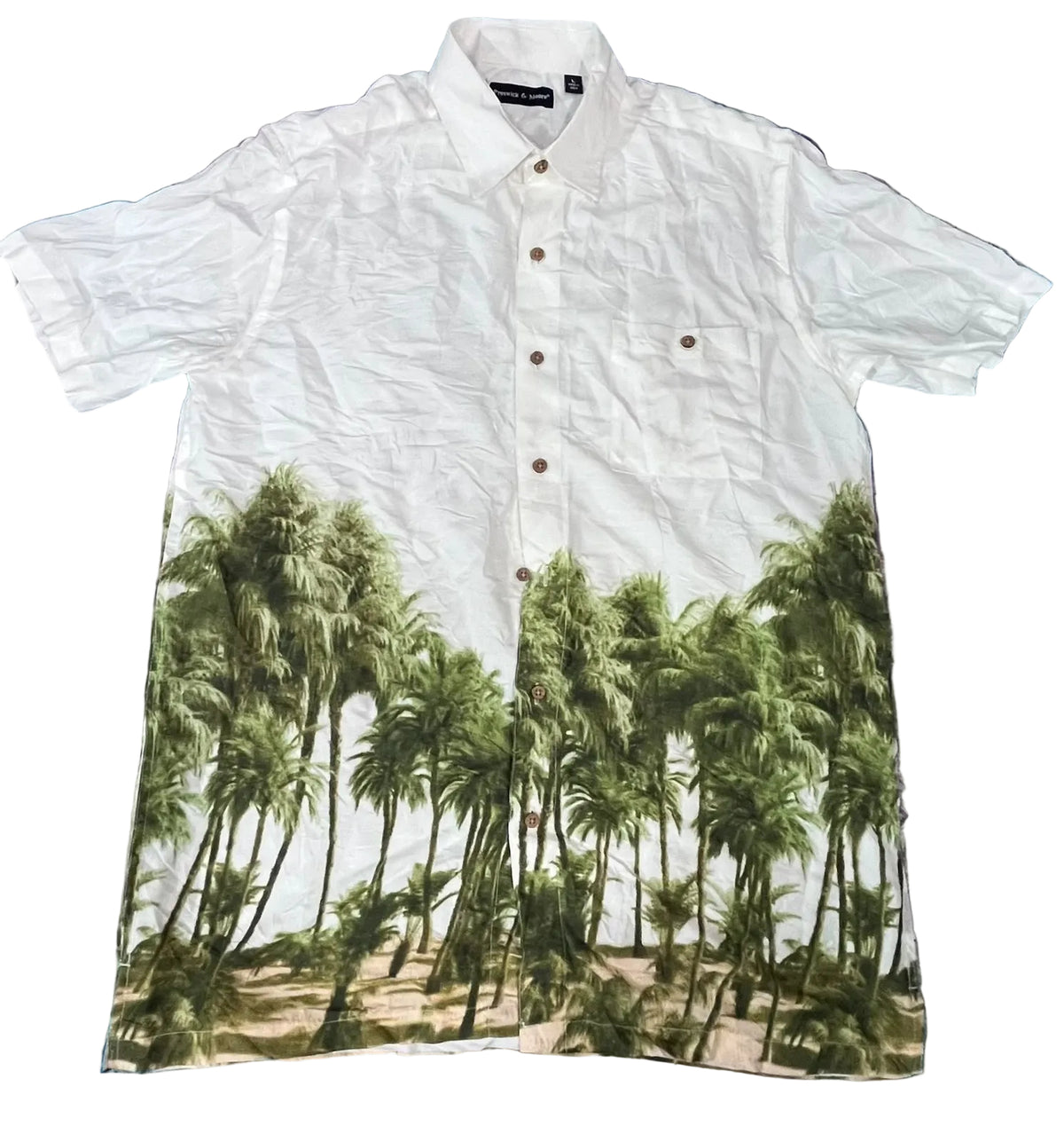 A white short-sleeve button-up shirt  The shirt features a printed graphic of green palm trees along the bottom half, with brown buttons and a black neck label.