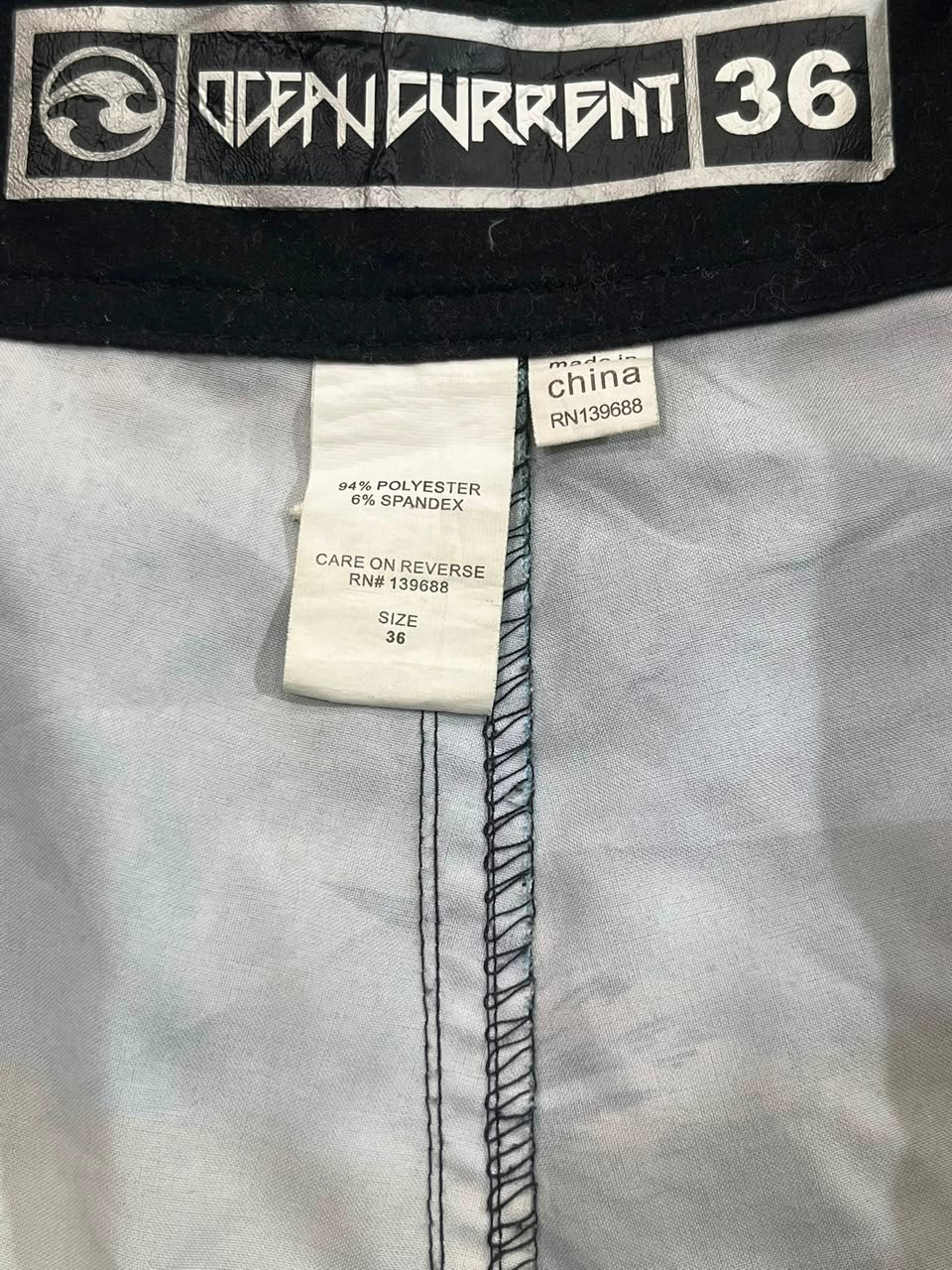 Close-up of the inside waistband of a pair of jeans, showing the black and white Ocean Current 36 brand label, a white care tag, and a small 'made in china' tag on the light gray fabric.