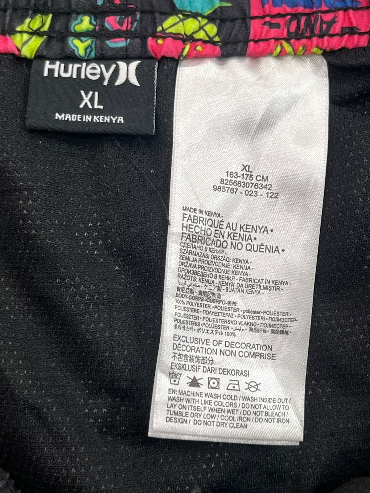 Close-up of a Hurley garment label and size information for an XL size item, with a black fabric body, colorful neon trim at the top, and a white care/information tag.