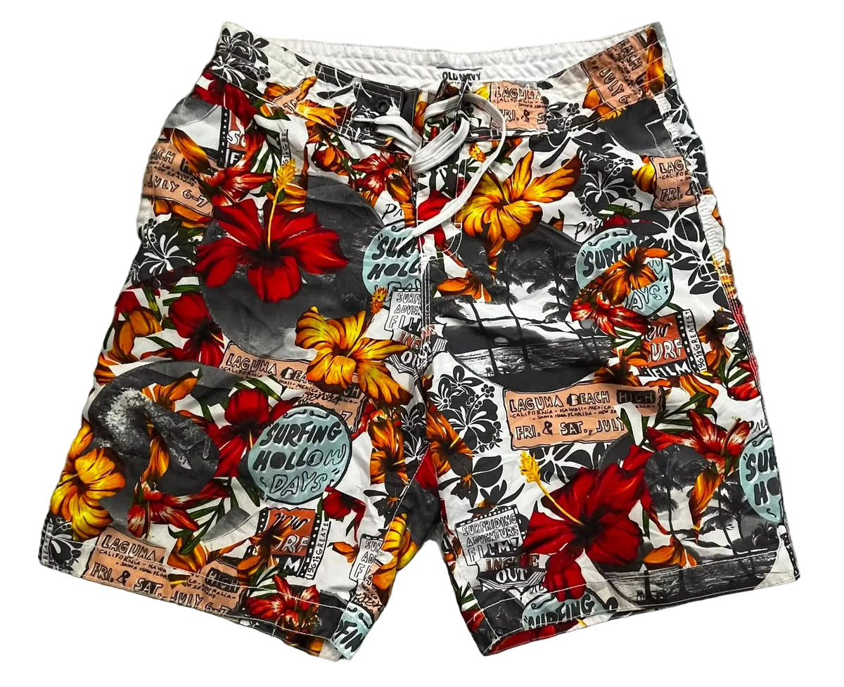 A pair of men's swim trunks featuring a busy collage print with red hibiscus flowers, yellow sunflowers, black-and-white graffiti-style murals, and vintage newspaper clippings,