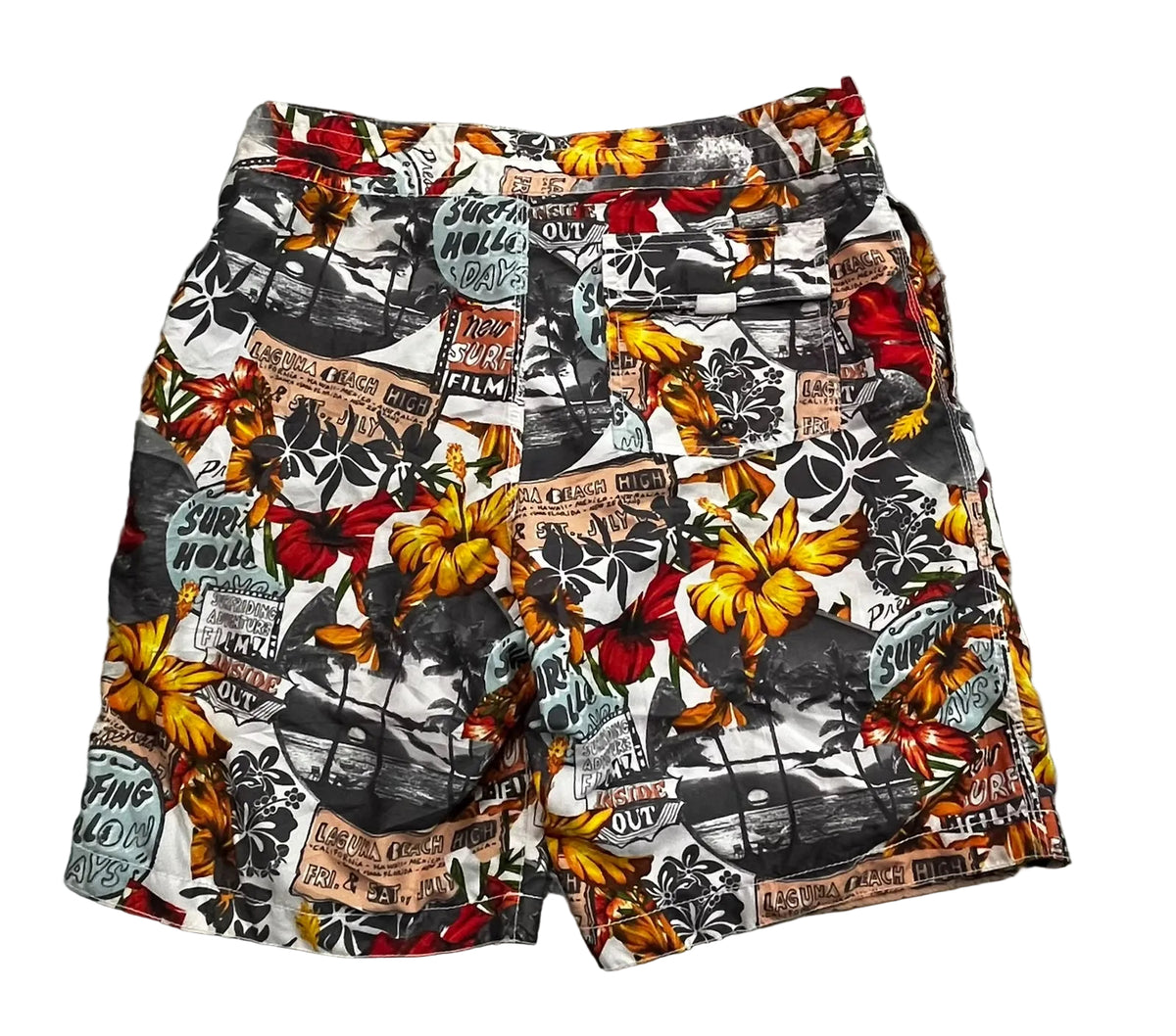 A pair of men's shorts featuring a busy, multicolor collage print with yellow hibiscus flowers, black-and-white beach scenes, and vintage-style newspaper clippings,