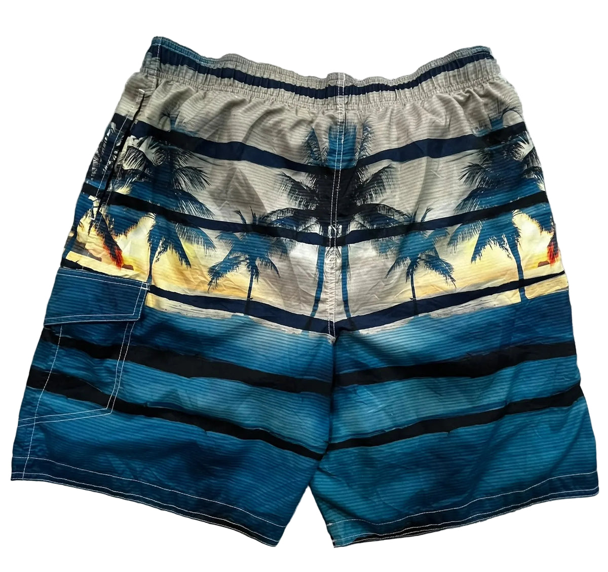 A pair of men's swim trunks featuring a tropical beach print with palm trees, sunset stripes, and blue ocean waves, 