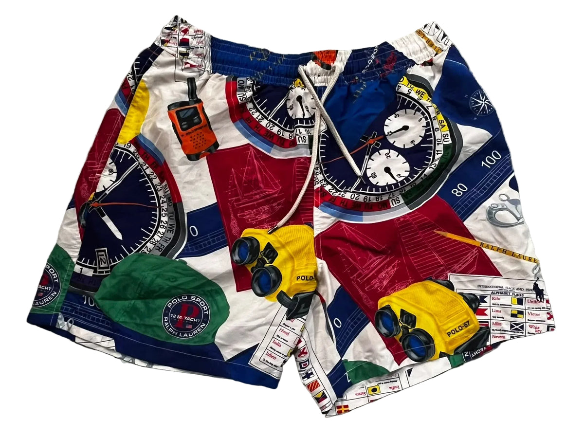 A pair of men's swim trunks featuring a colorful nautical-themed print with compasses, binoculars, a sextant, and nautical charts,