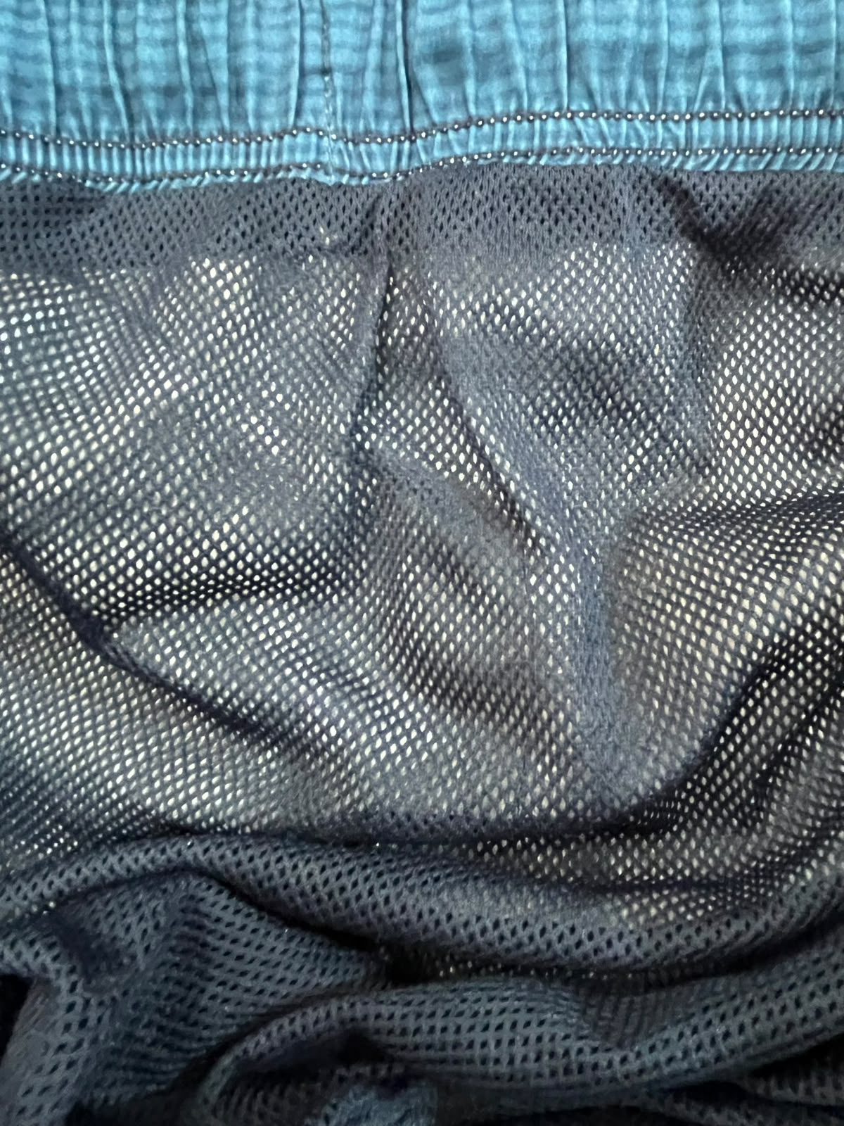 Close-up of a dark gray mesh fabric with a lighter blue elastic waistband.