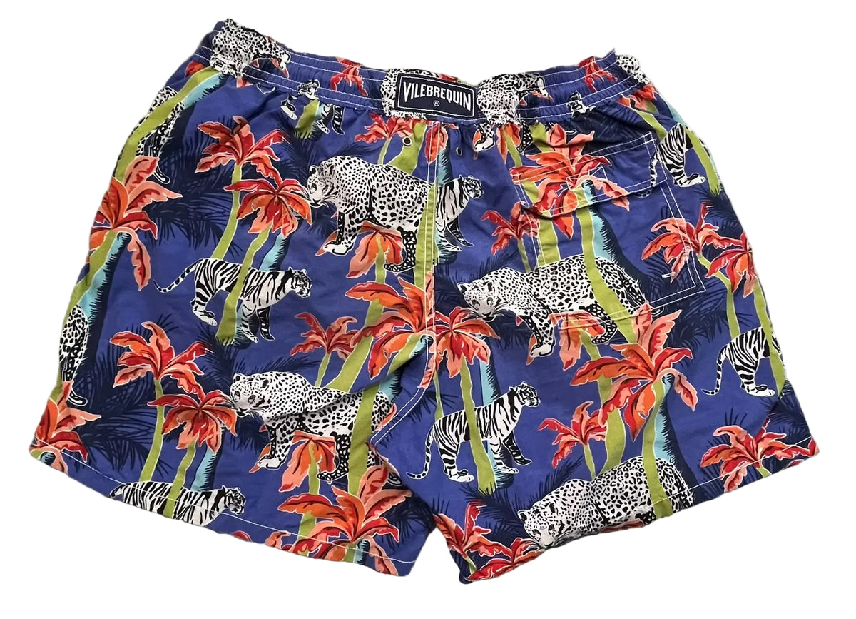 Vilebrequin men's swim trunks featuring a vibrant blue tropical print with red palm leaves, green palm trunks, and spotted leopards and zebras,