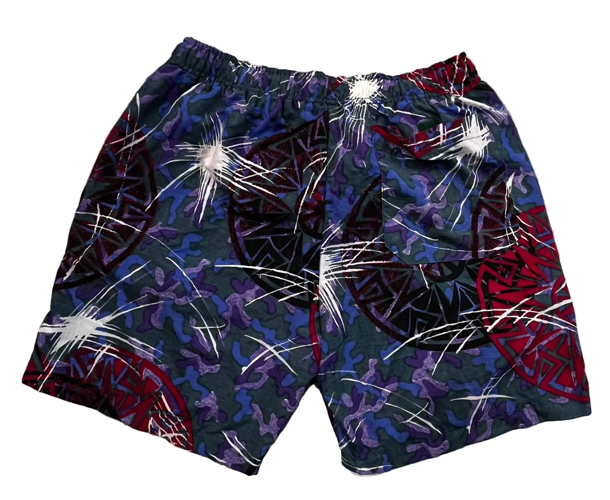 A pair of men's swim trunks featuring a complex abstract pattern with purple, red, black, and white elements, 