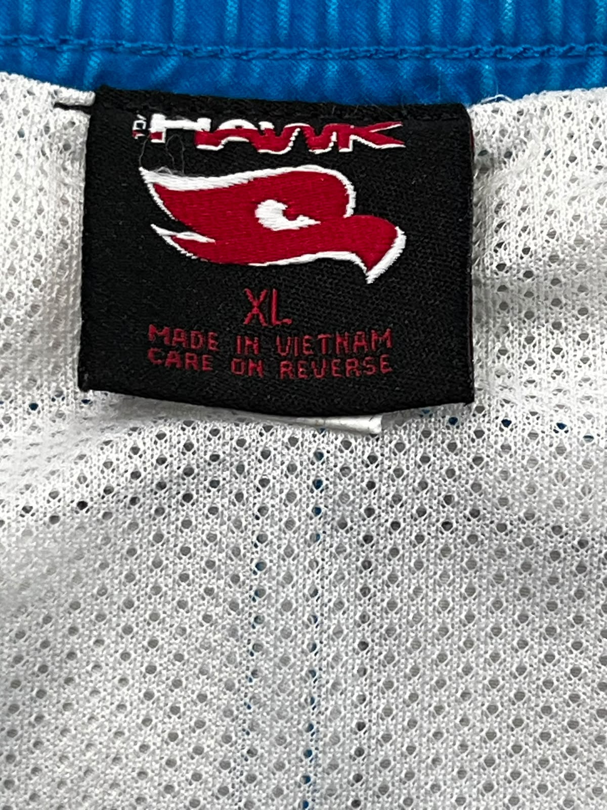 Close-up of a black embroidered athletic tag on a white mesh garment, showing the red and white Navy logo and text including 'XL' and 'MADE IN VIETNAM'.