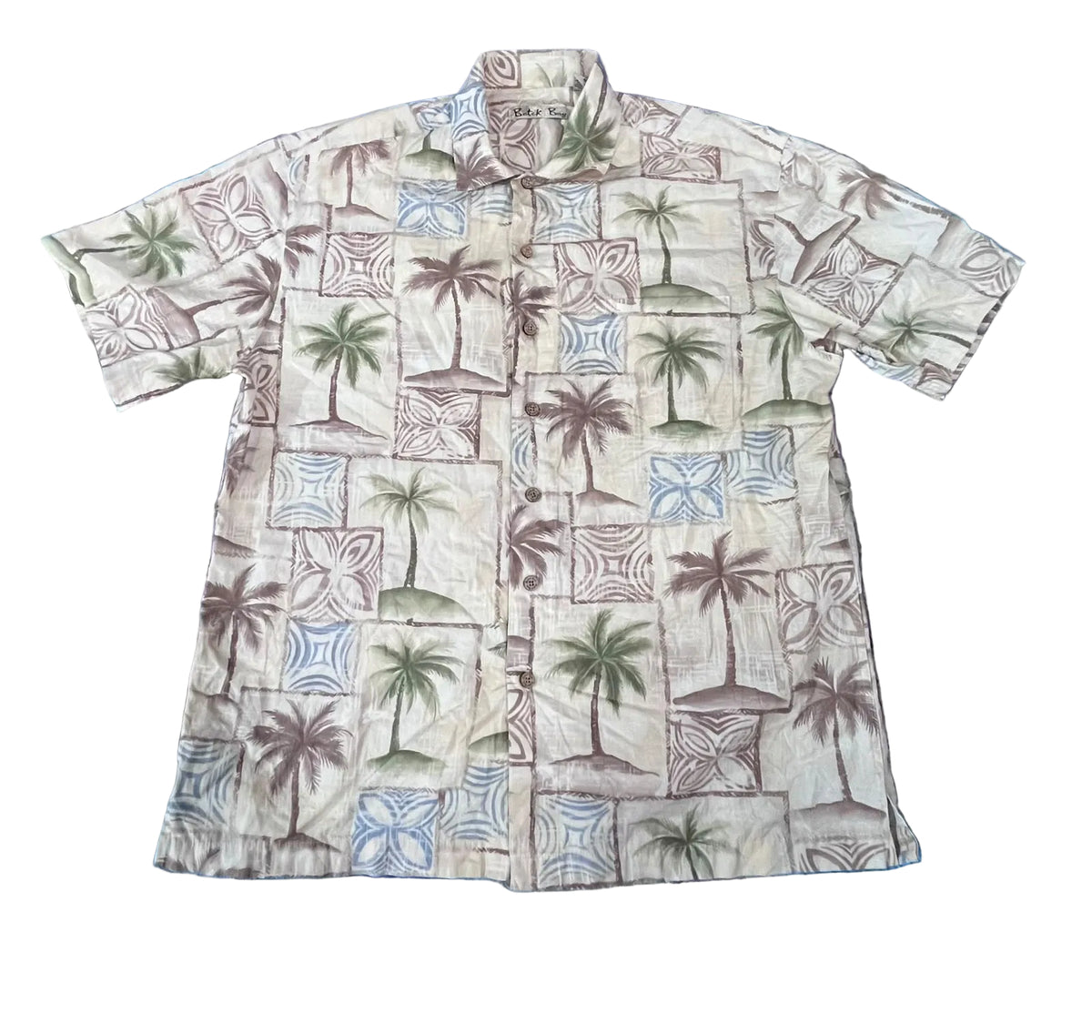 A short-sleeve button-up camp shirt with a tropical print featuring palm trees, beach umbrellas, and geometric tiles in muted green, blue, and brown on a cream background, 