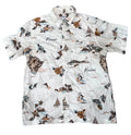 A white short-sleeve button-up Hawaiian shirt with a colorful tropical print featuring hula dancers, sailboats, palm trees, and the word 'Hawaii'