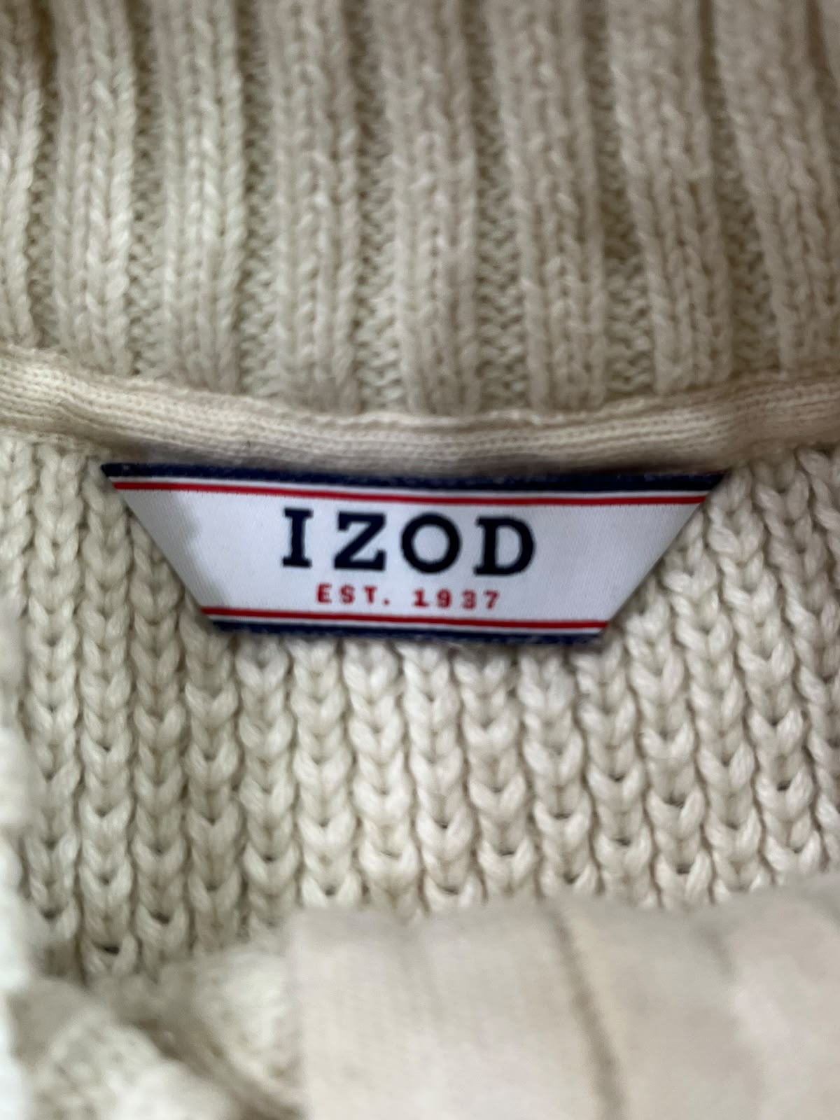 Close-up of a cream-colored ribbed knit garment with a visible Izod brand label.