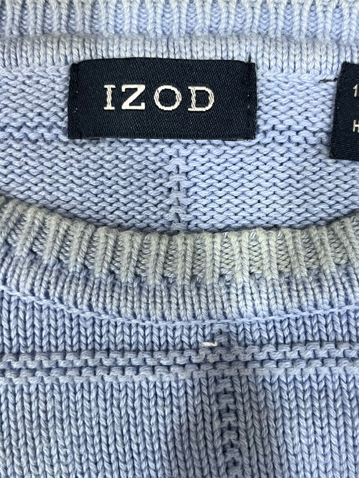 Close-up of a light blue knitted garment with a black fabric label reading 'IZOD' in white text.