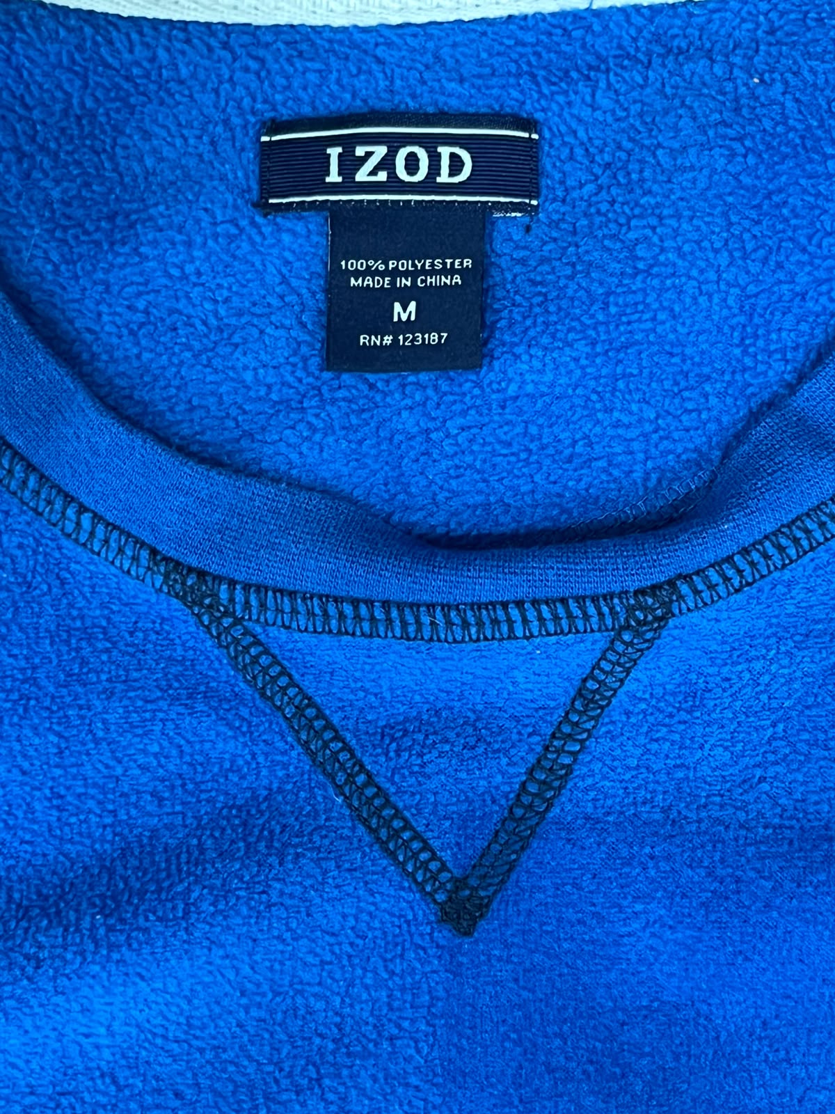 Close-up of a bright blue fleece garment with a visible black Izod neck label and black contrast stitching.
