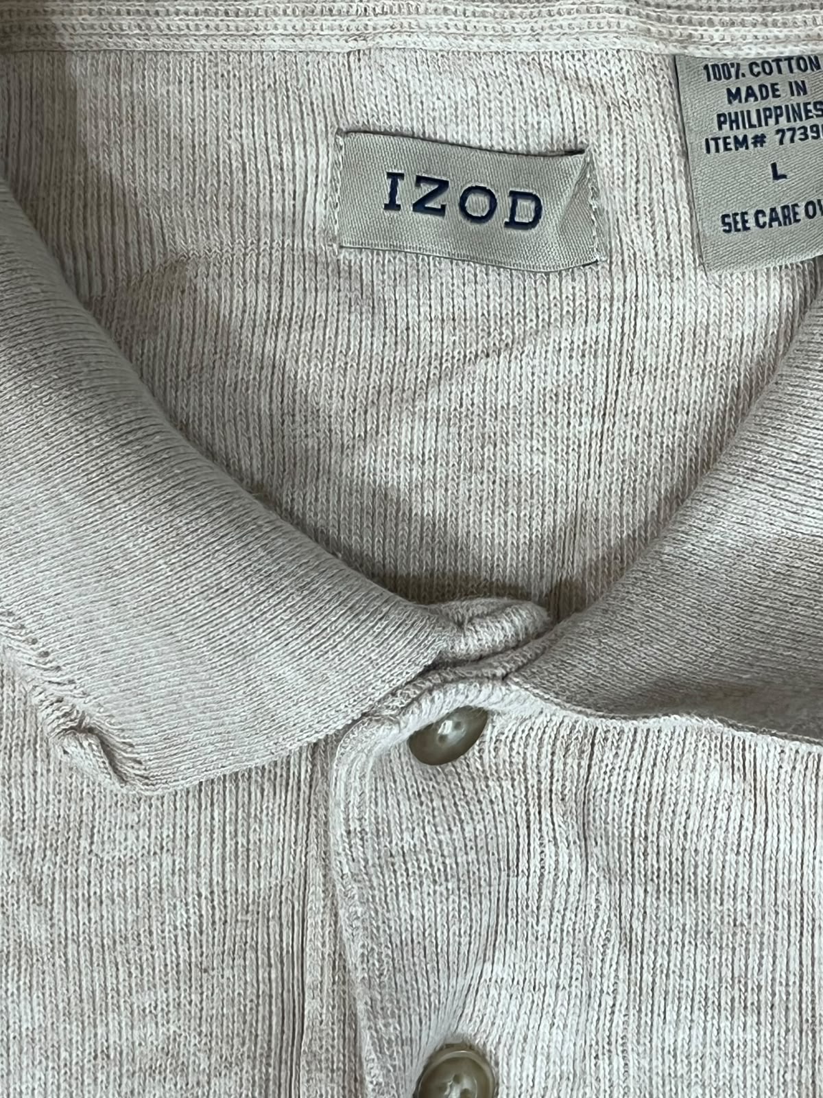Close-up of a light beige ribbed knit polo shirt collar with the brand label 'IZOD' visible, plus a sewn-back care label.