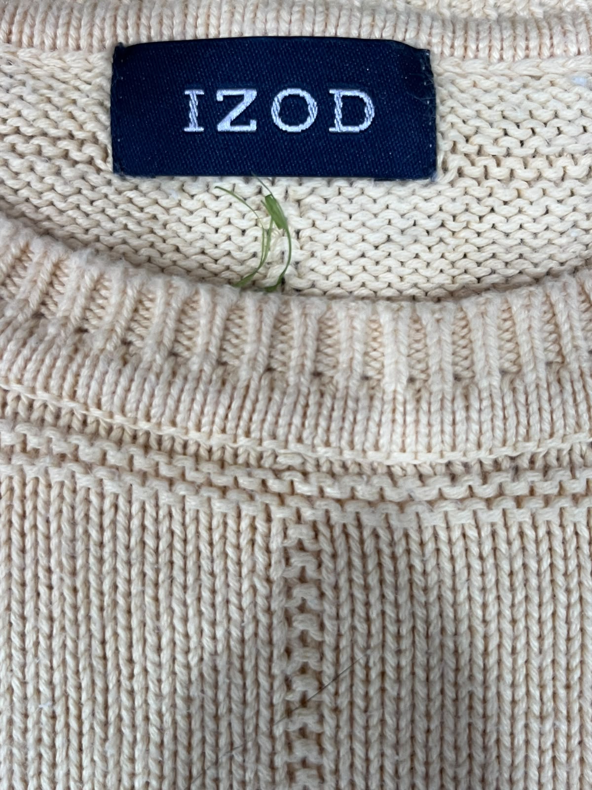 Close-up of a cream-colored knit sweater with a dark navy blue brand label reading 'IZOD' at the collar.