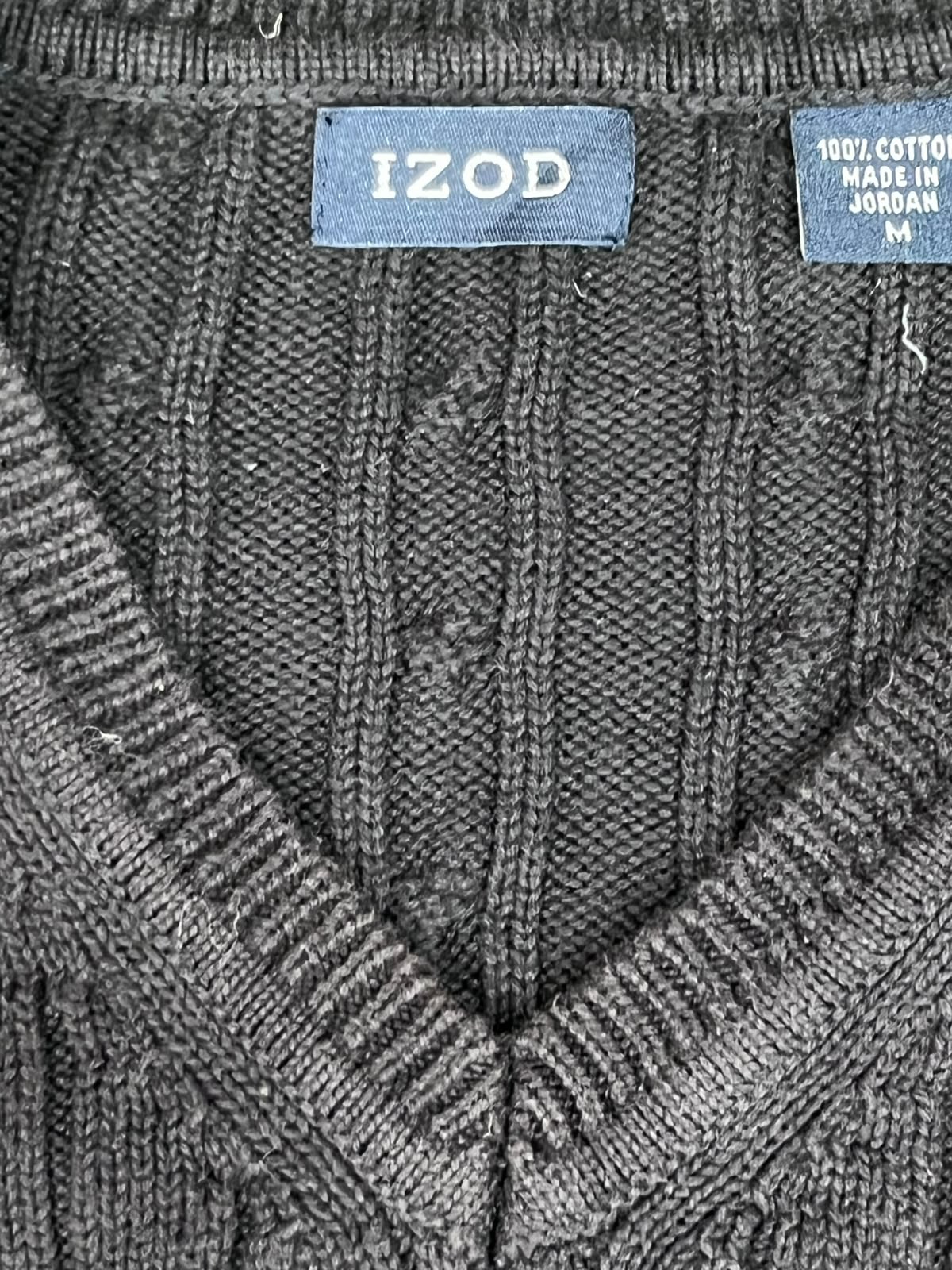 Close-up of a dark gray ribbed knit sweater with a V-neck, showing a blue 'IZOD' brand label and a '100% COTTON MADE IN JORDAN' tag at the collar.