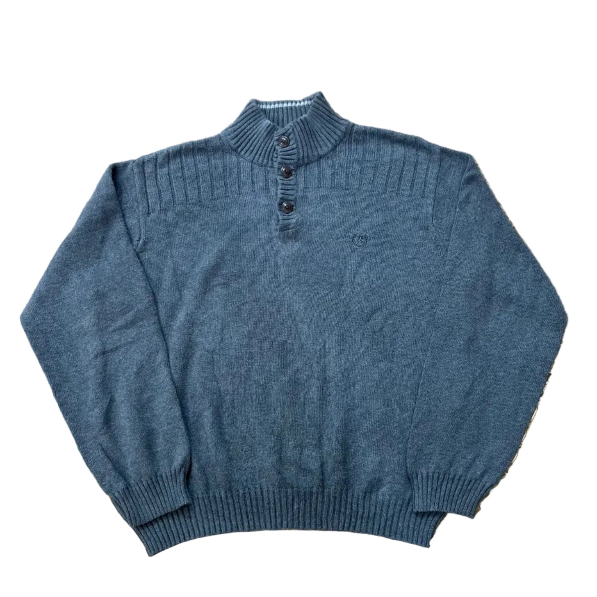 A dusty slate blue knit mock-neck sweater with three dark buttons, a white background. A pair of bare feet is visible at the bottom edge of the frame.