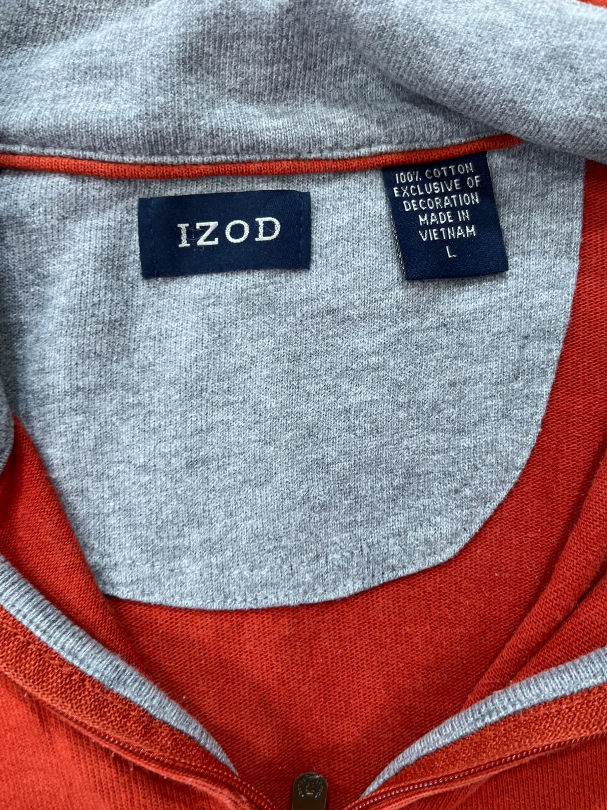 Close-up of the inside collar of a gray knit top with a red-orange undershirt or layer visible at the neckline. Two brand labels are visible: a central navy Izod label and a smaller black care/origin label reading '100% COTTON EXCLUSIVE OF DECORATION MADE IN VIETNAM L'.