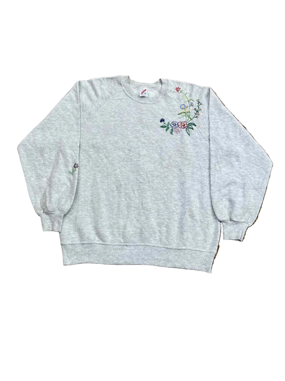 A light heather gray sweatshirt with colorful floral embroidery on the lower right chest,