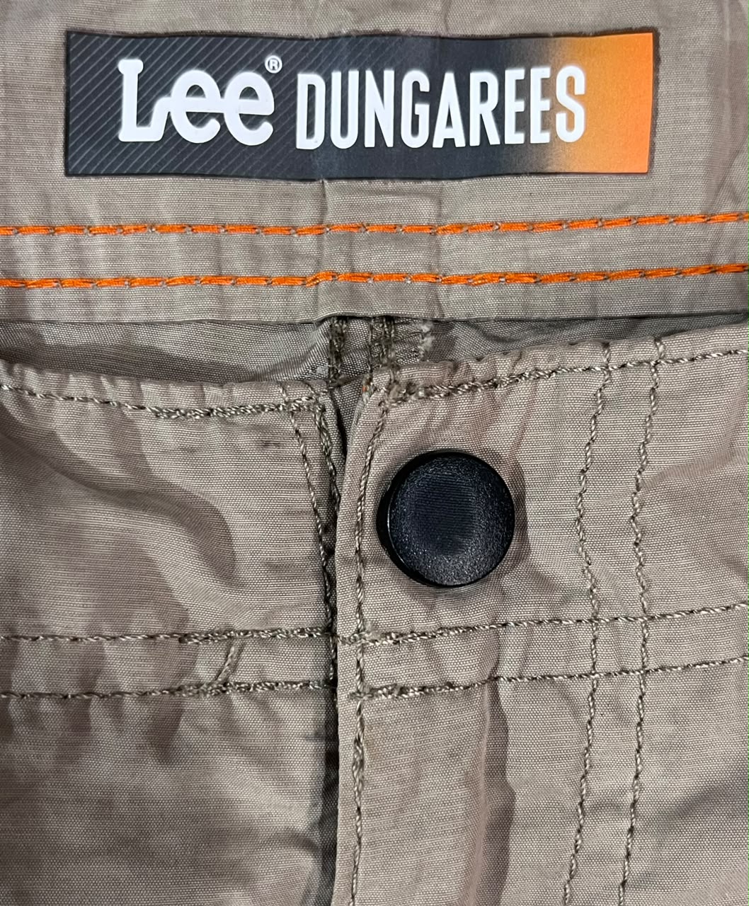 Close-up of Lee Dungarees workwear trousers showing the interior waistband, orange contrast stitching, a black button closure, and the Lee Dungarees brand label.