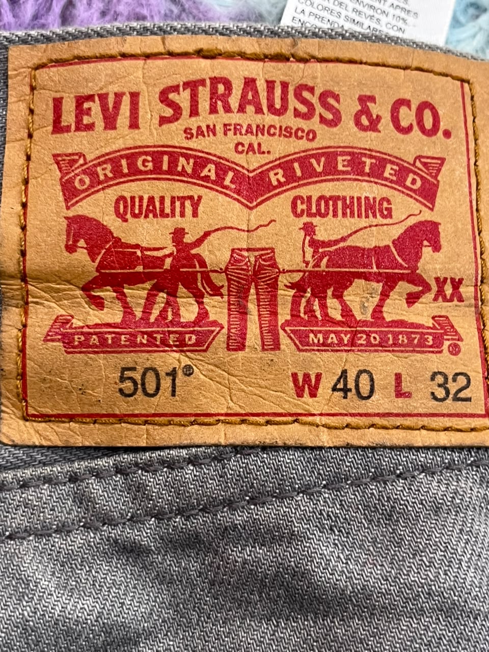 Close-up of a vintage Levi's 501 waistband label sewn onto gray denim fabric, showing the red printed Levi Strauss & Co. branding and size information.