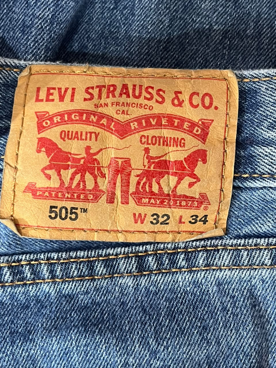 Close-up of a Levi's 505 waistband patch on blue denim jeans, showing the tan leather brand label with red text and horse-and-pants graphics.