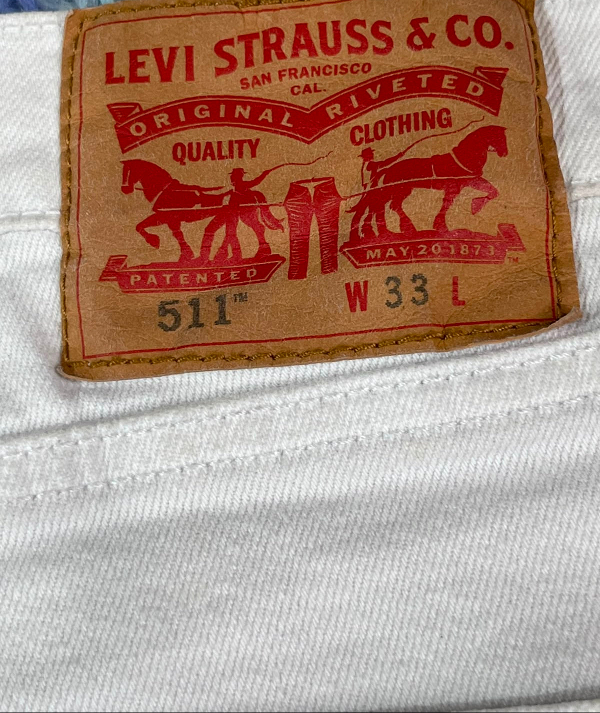A close-up of a vintage-style Levi's 511 waistband label sewn onto off-white denim fabric. The tan leather patch features red printed text and horse-and-carriage graphics with the brand name 'Levi Strauss & Co.
