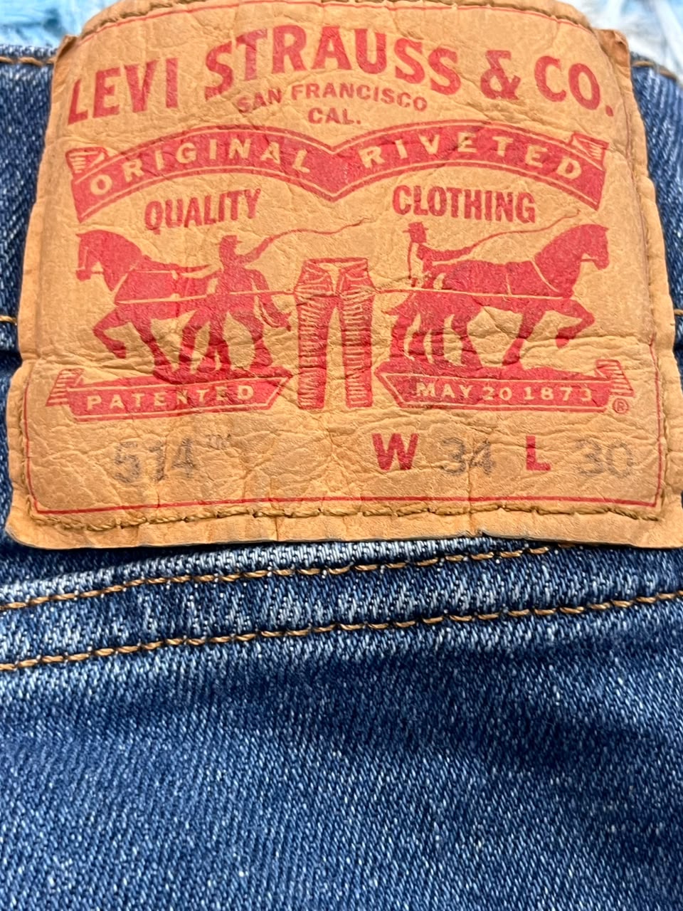 Close-up of a vintage Levi's riveted leather patch on blue denim jeans, showing red printed branding and horse-and-pants graphics.