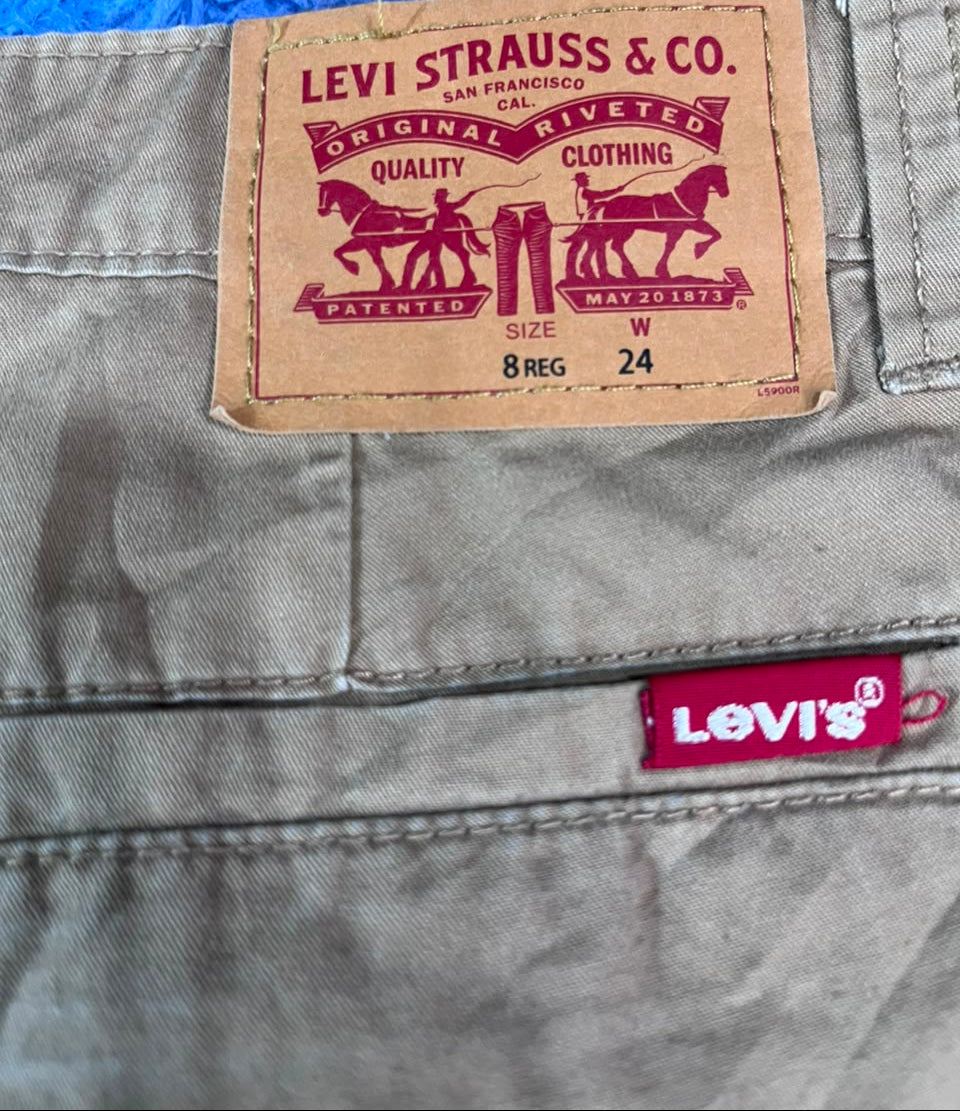 Close-up of Levi's pants showing the tan leather back waistband label with the classic horse-and-carriage logo and text, plus a small red Levi's brand tab on the lower right.