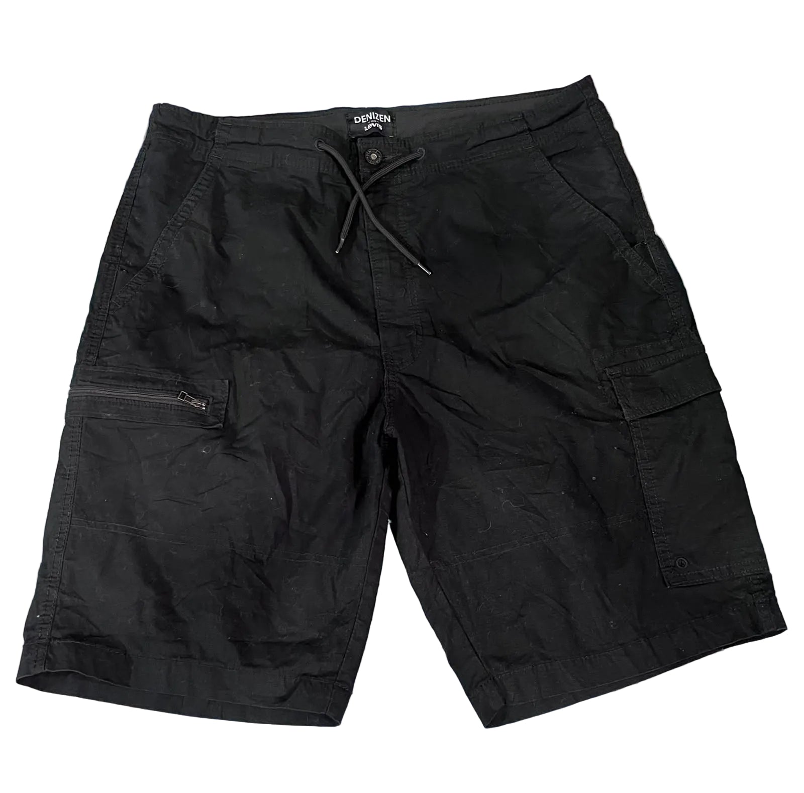 Black cargo shorts with a drawstring waist and zippered side pocket, laid flat on a colorful textured rug.