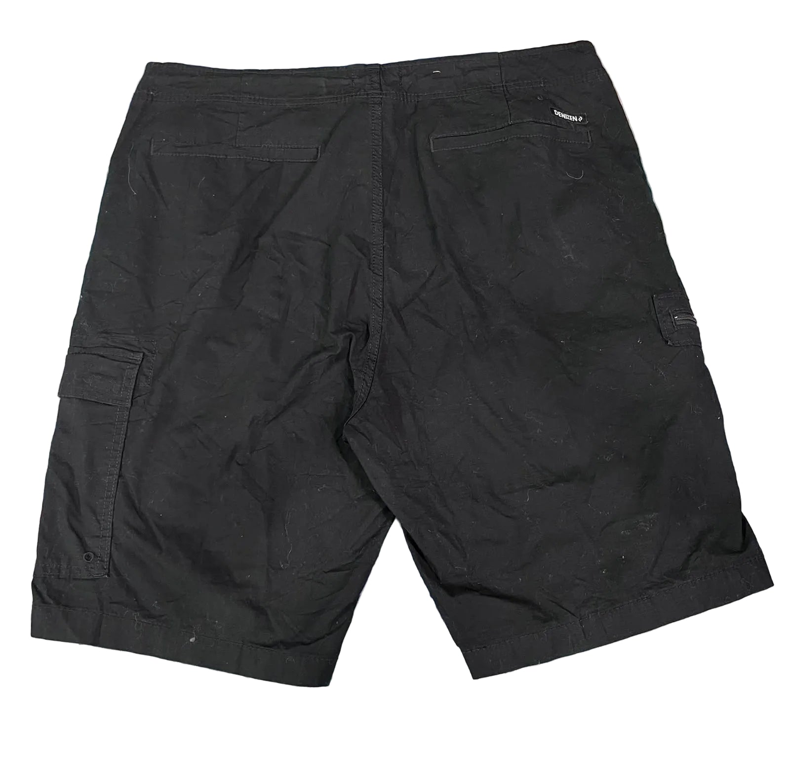 Black cargo shorts laid flat on a colorful, textured shag rug. The shorts feature side cargo pockets and a small white brand tag on the back waistband.