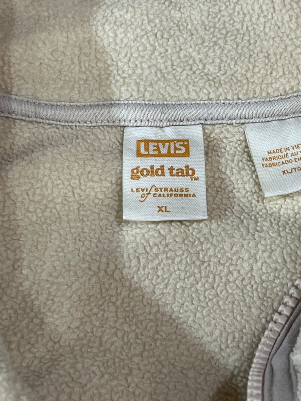 Close-up of a Levi's garment interior showing the brand tag on a textured fleece fabric. The tag reads 'LEVI'S gold tab LEVI'S STRAUSS OF CALIFORNIA' and indicates size XL.