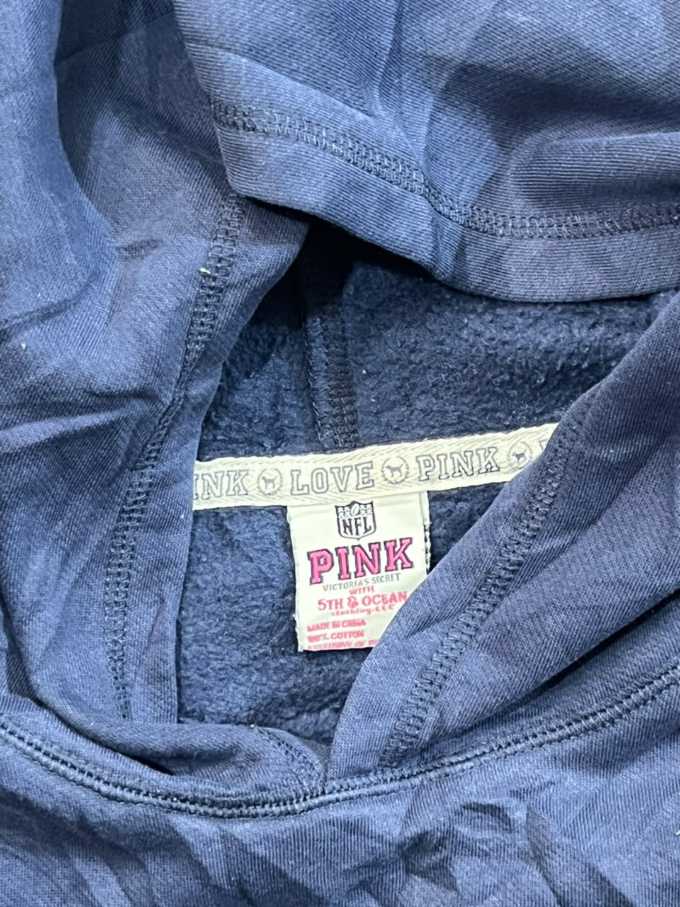 Close-up of a blue fleece-lined hoodie or sweatshirt interior showing a sewn-in label that reads PINK LOVE PINK with NFL branding.