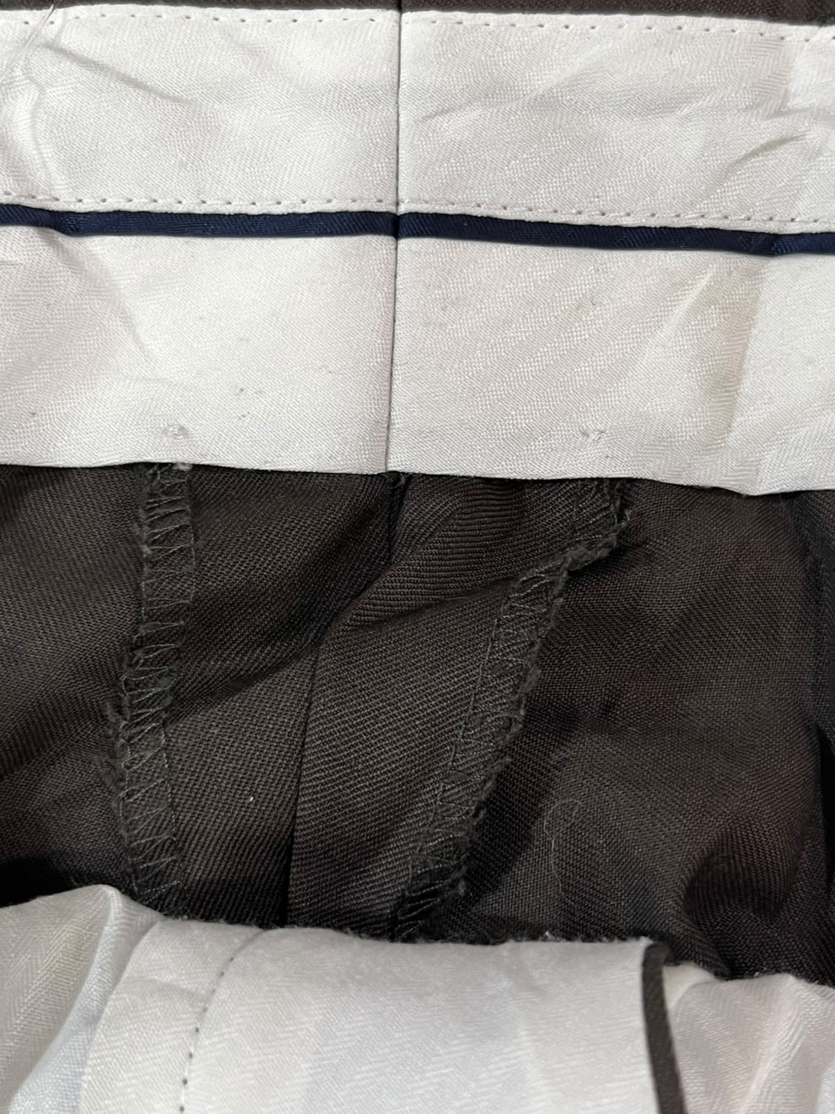 Close-up detail of a garment showing a white fabric cuff with a thin dark stripe, a dark brown or black textured lining, and white stitched fabric at the bottom.