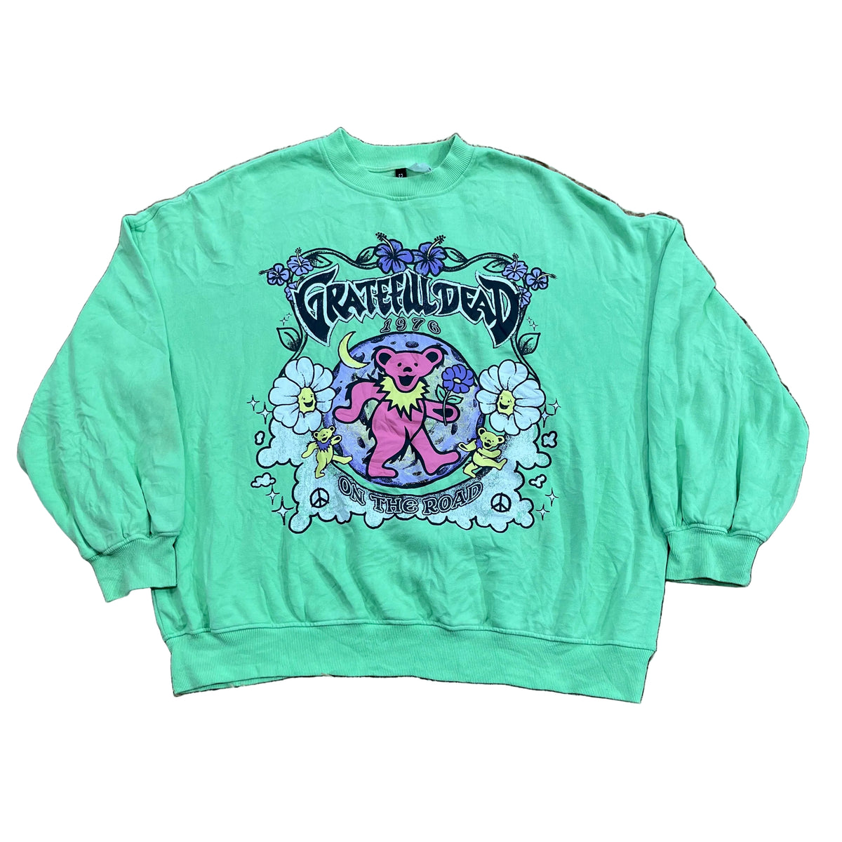 A mint green long-sleeve t-shirt with a colorful Grateful Dead 'The Moon Is Down' graphic, . A person's foot is visible on the left edge of the frame.