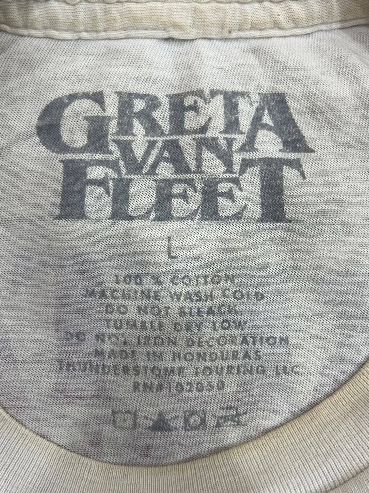 Close-up of the inside neck label of a vintage Greta Van Fleet band t-shirt, showing the size L and care instructions on a light beige cotton fabric.