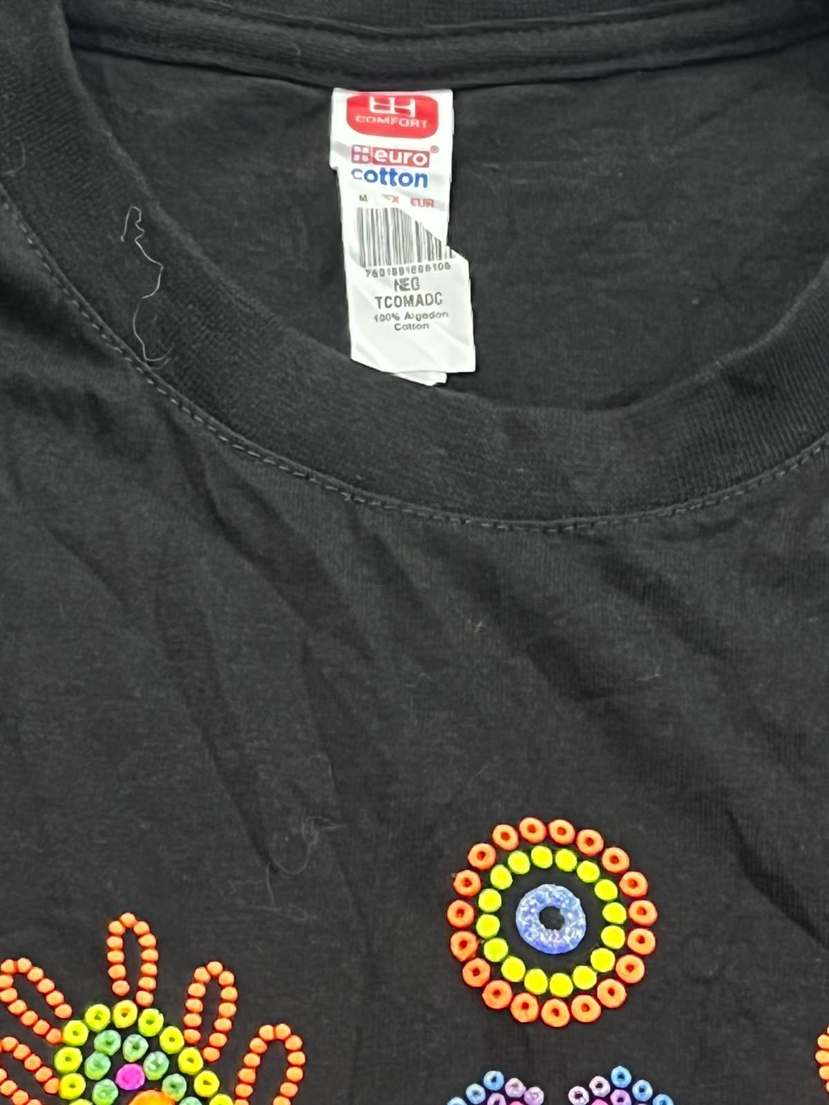 Close-up of a black cotton t-shirt featuring colorful beadwork-style circular and floral patterns on the front, with a visible Hanes neck label.