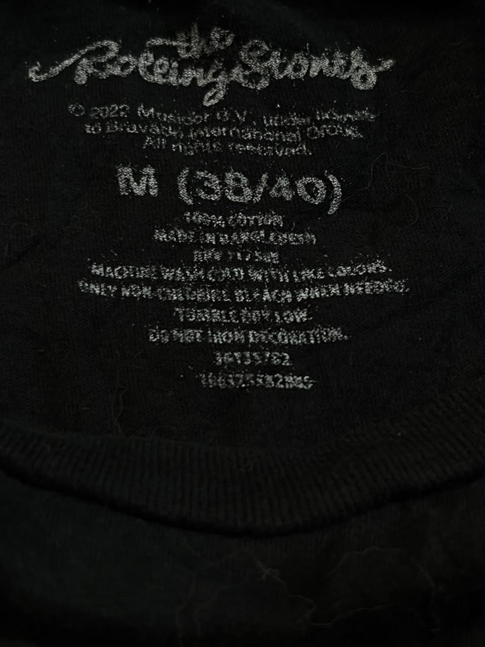 Close-up of a black garment label reading 'The Rolling Stones' in white script, with size information 'M (38/40)' and care text below.