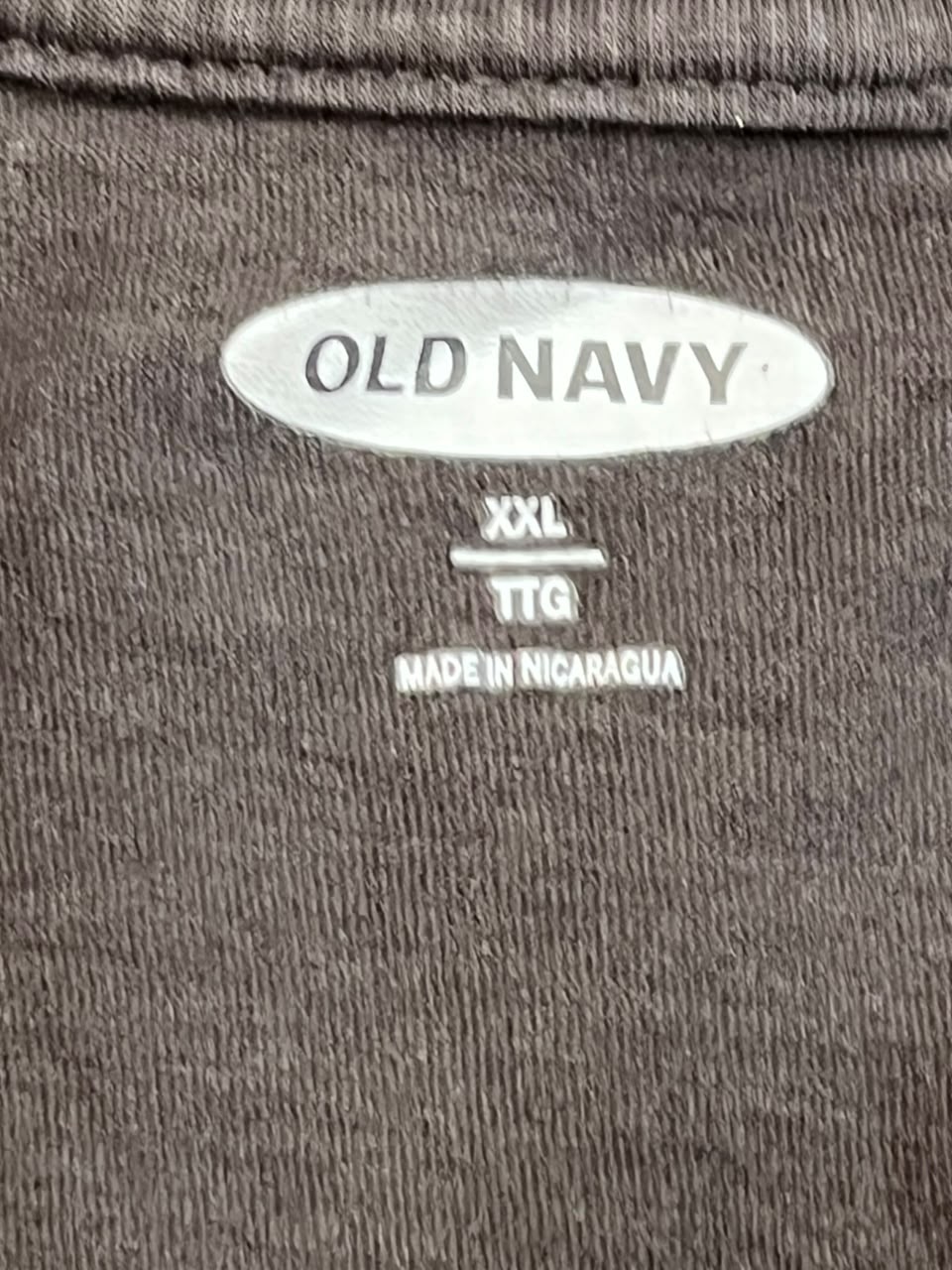 Close-up of a dark brown ribbed fabric label reading OLD NAVY, with size information XXL TTG and MADE IN NICARAGUA printed below.