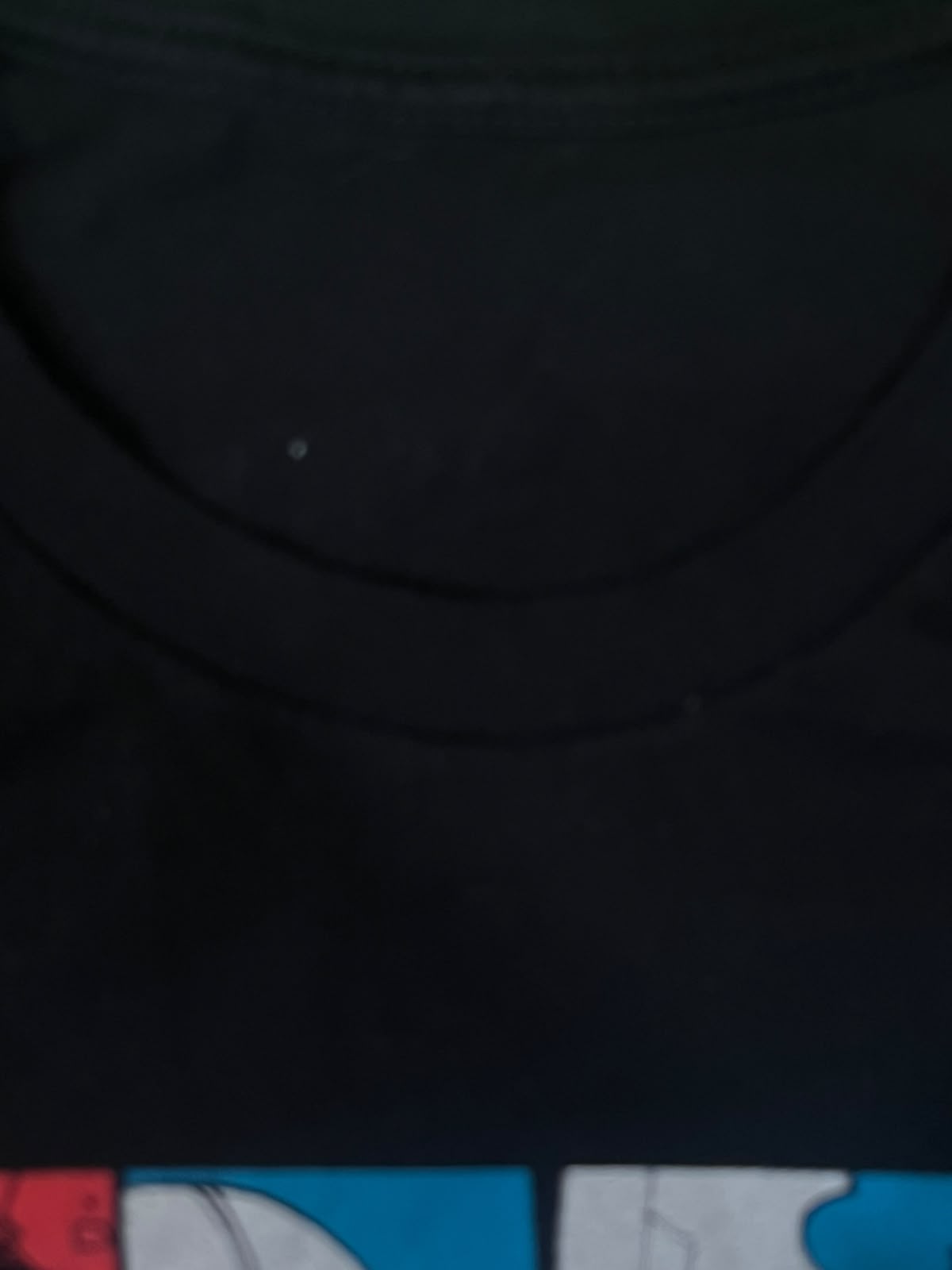 Close-up of a black crew-neck t-shirt showing the inner collar area and part of a colorful graphic print at the bottom.