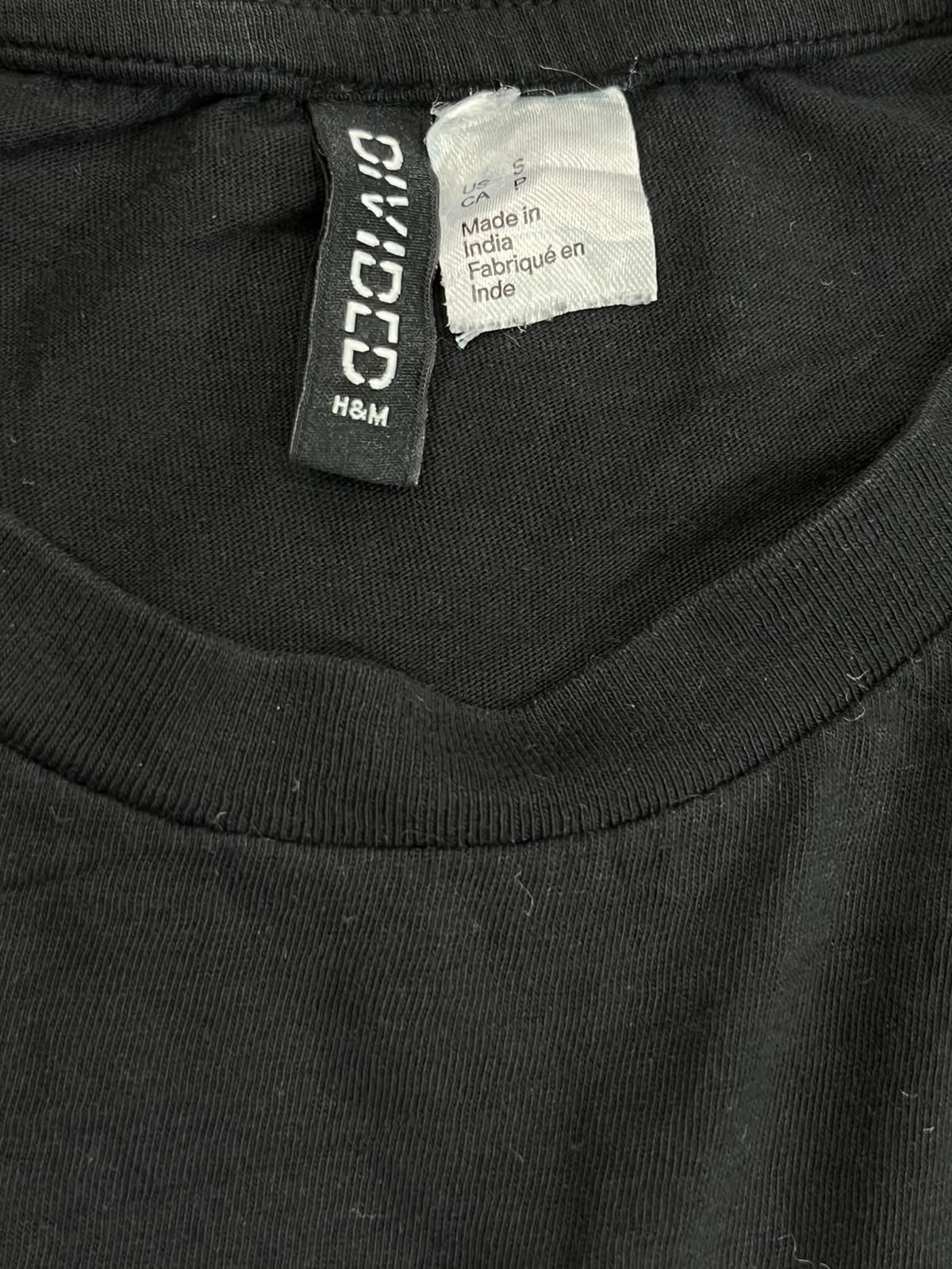 Close-up of a black crewneck t-shirt showing the inner neck labels, including a black 'DIVIDED H&M' brand tag and a white 'Made in India' care label.