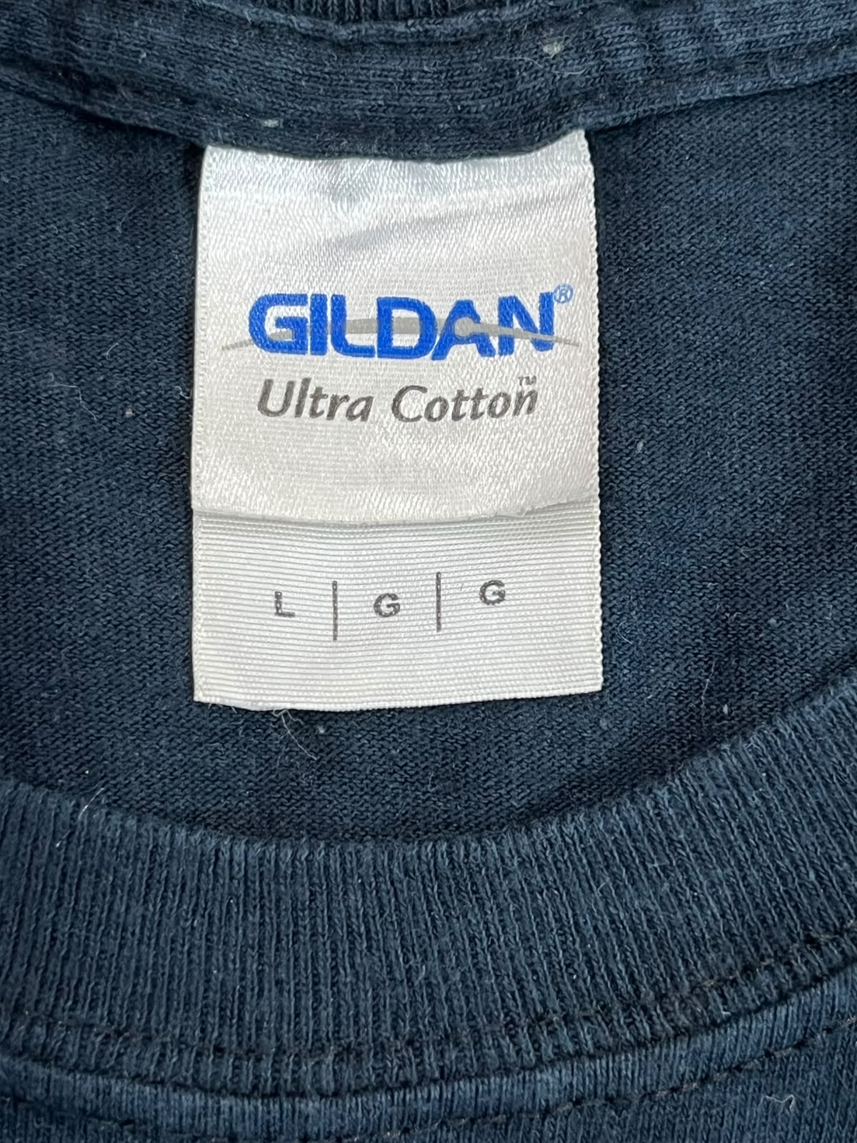 Close-up of a Gildan Ultra Cotton t-shirt neck label on a dark navy blue ribbed fabric.