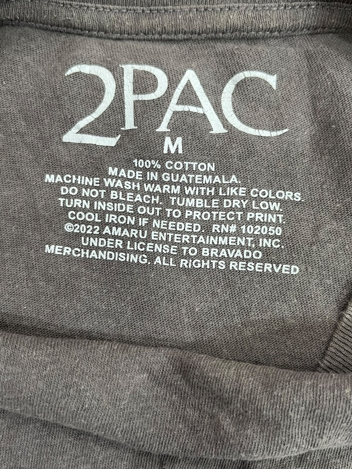Close-up of a gray 2PAC t-shirt label showing the brand name '2PAC' in large white letters and care instructions printed below.