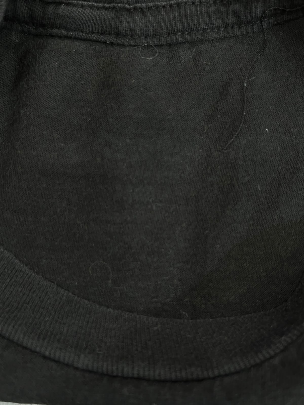 Close-up of a black ribbed knit fabric, showing the texture and neckline stitching.
