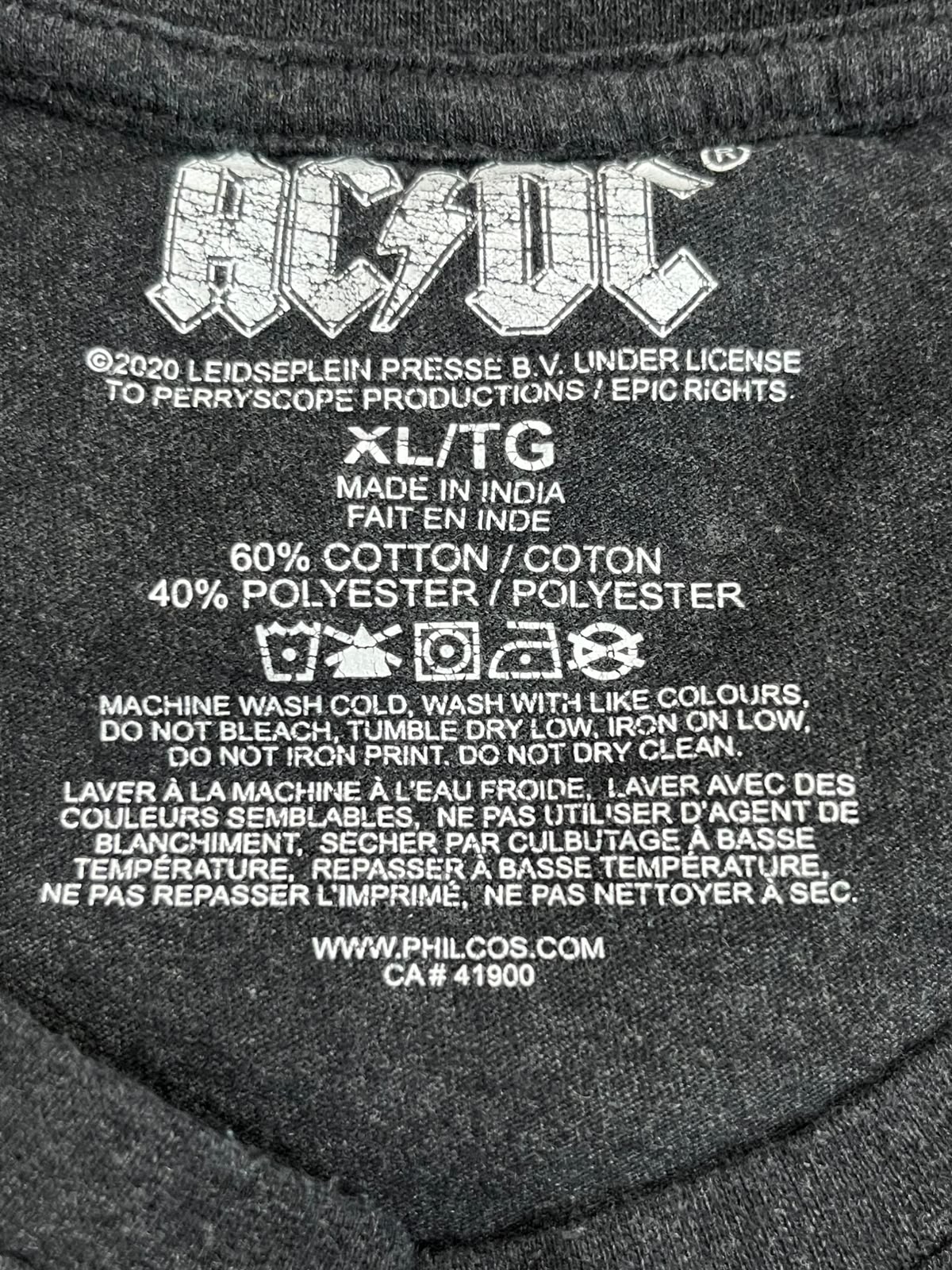 Close-up of the inside neck label of a dark gray AC/DC t-shirt, showing the band logo, size XL/TG, material composition, care instructions, and website PHILCOS.