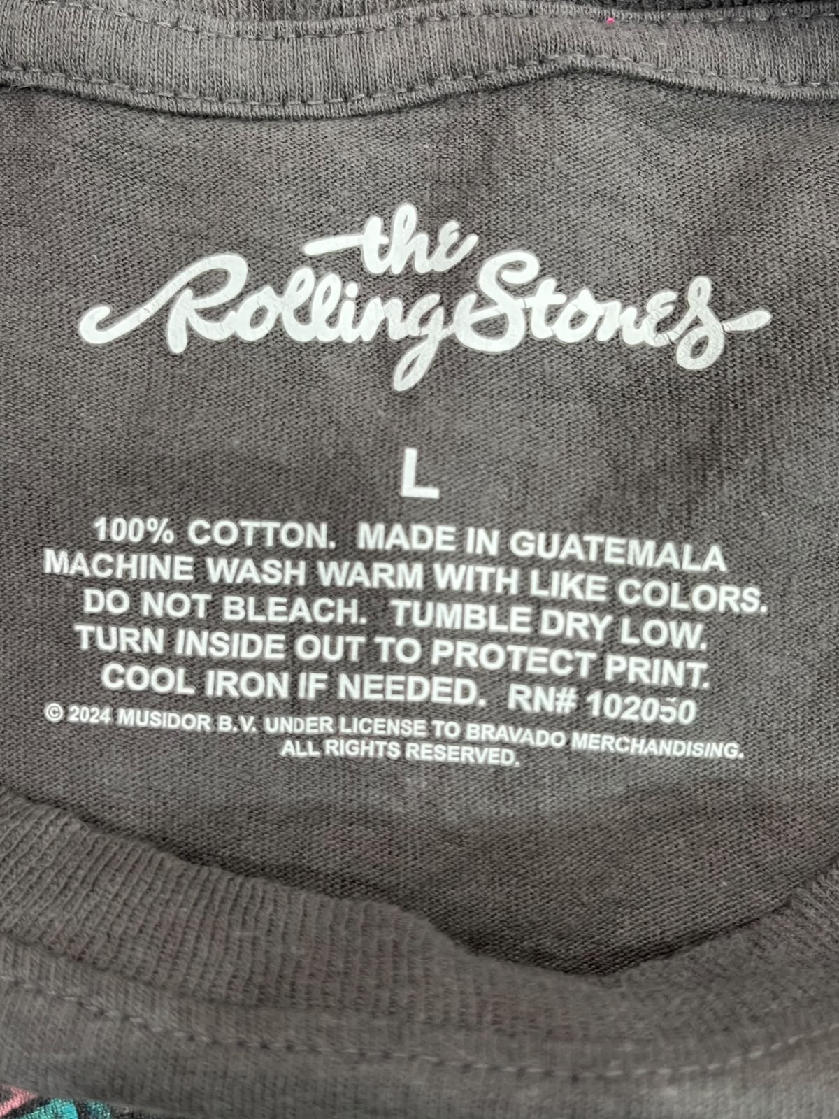 Close-up of the inside collar of a dark gray t-shirt featuring white printed text with 'the Rolling Stones' logo and size information.